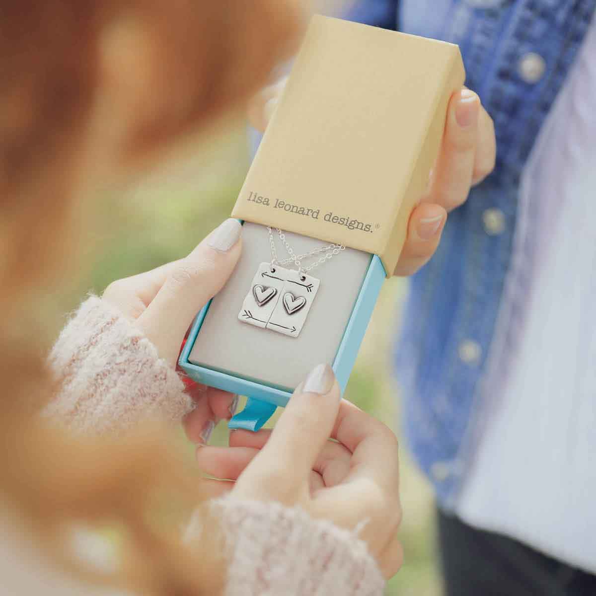 girl giving another girl the sterling silver i love you necklace set in a lisa leonard box