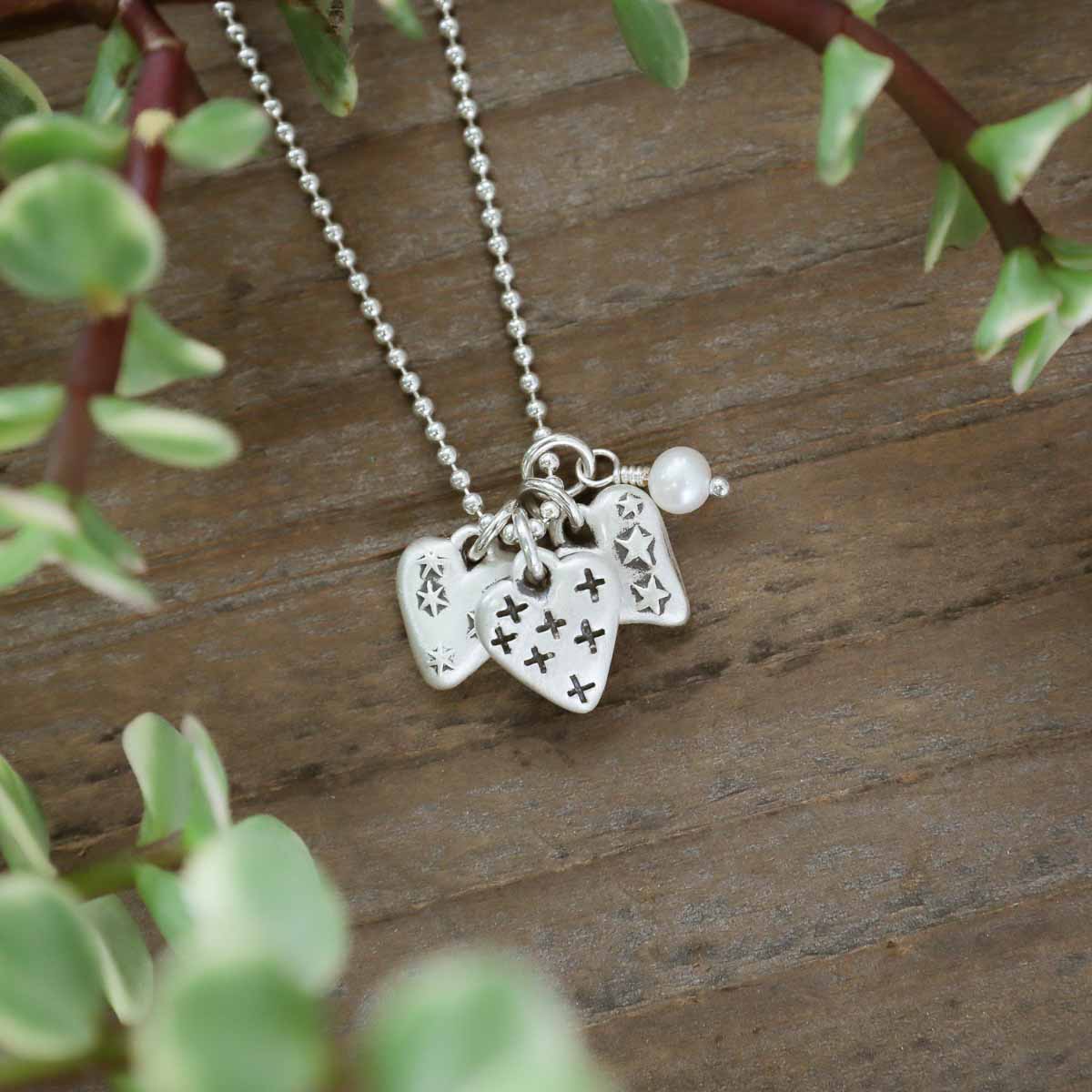 Light + Bright hearts necklace handcrafted in sterling silver with a matte brushed finish and the heart charm hung next to a vintage freshwater pearl