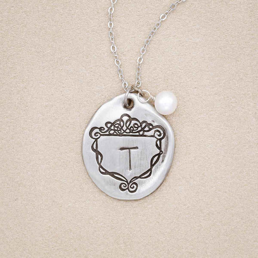 A Family Crest necklace handcrafted in pewter, customized with an initial and includes a freshwater pearl