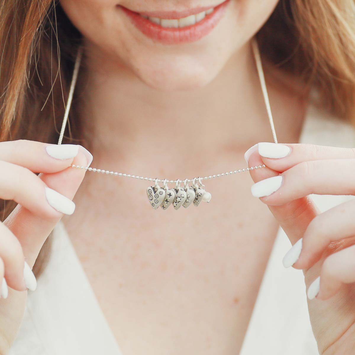 Girl wearing her Light + Bright hearts necklace handcrafted in sterling silver with a matte brushed finish and the heart charm hung next to a vintage freshwater pearl