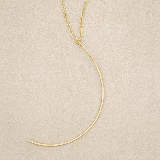 A gold filled New Moon Necklace, on beige background
