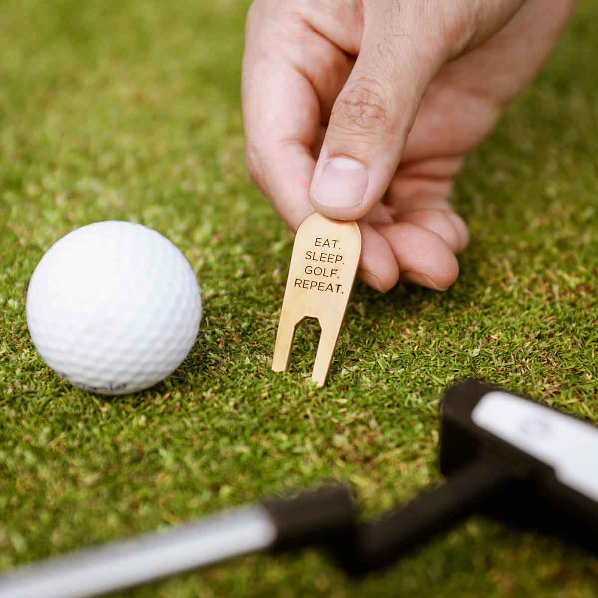 hand holding bronze personalized divot tool next to a golf ball