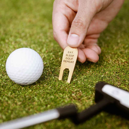 hand holding bronze personalized divot tool next to a golf ball