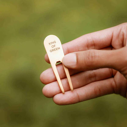 hand holding bronze personalized divot tool on a golf course