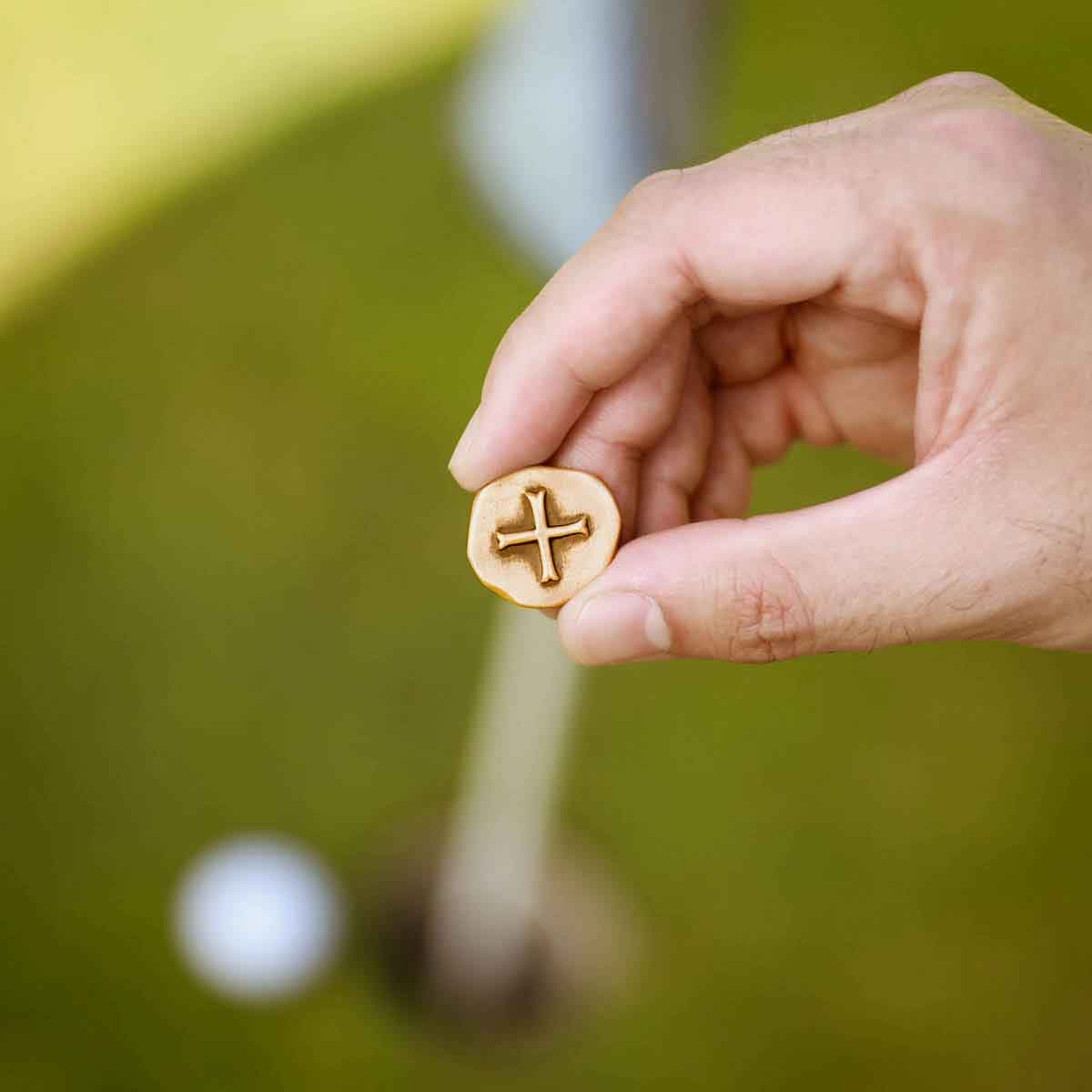 hand holding Bronze Roman Cross Coin Golf Ball Marker